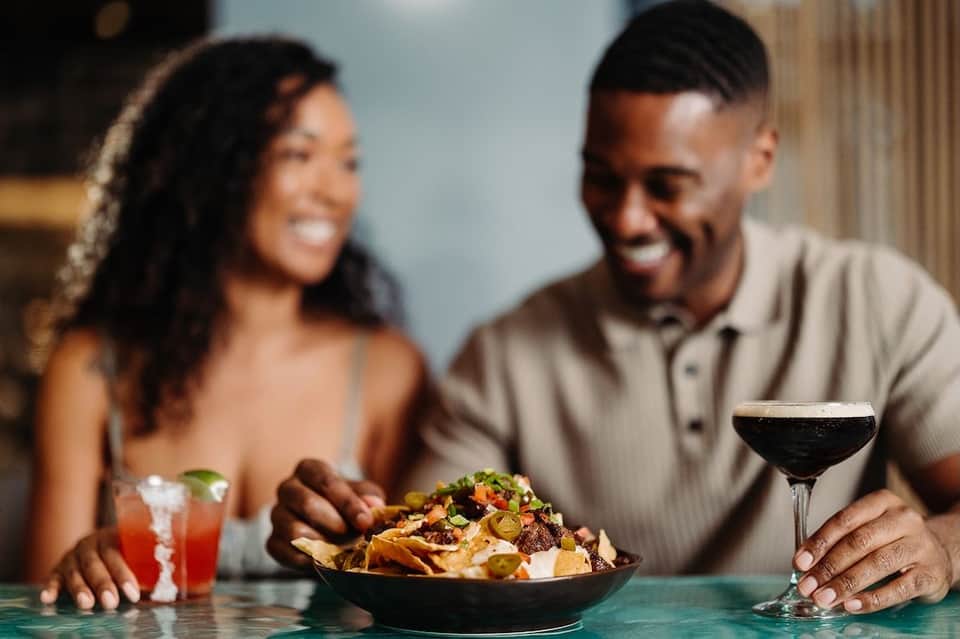 Couple enjoying appetizers and cocktails at a restaurant bar with focused plating and elegant glassware