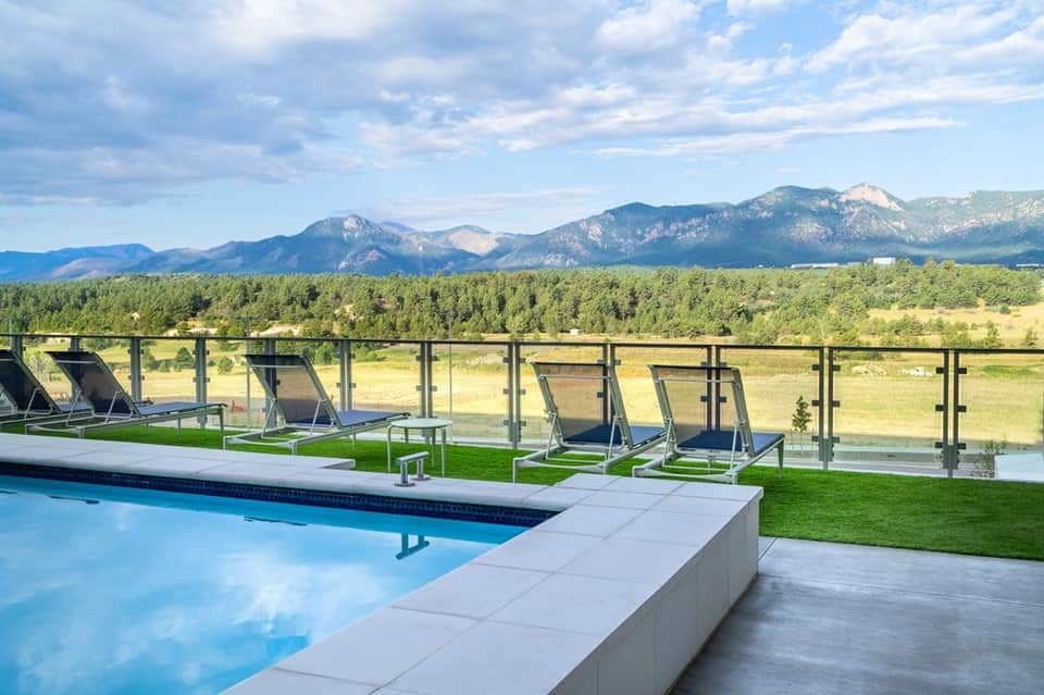 Modern resort pool with loungers, glass railing, and mountain range vista beyond