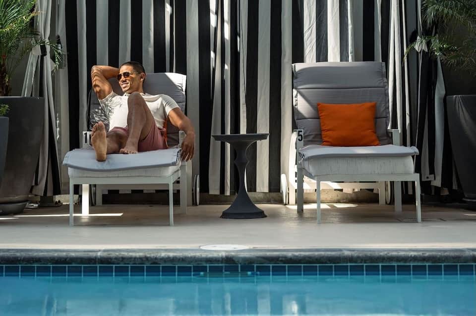 Guest relaxing on poolside lounge chair with striped privacy screens and pool view