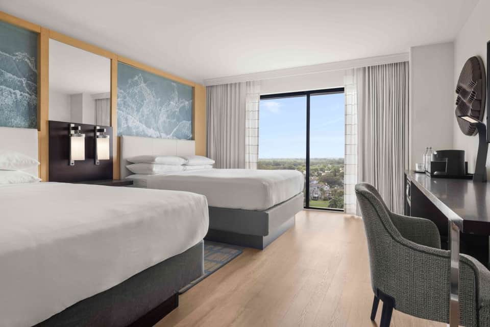Modern hotel room with two queen beds, ocean view balcony, wooden accents, and contemporary furnishings