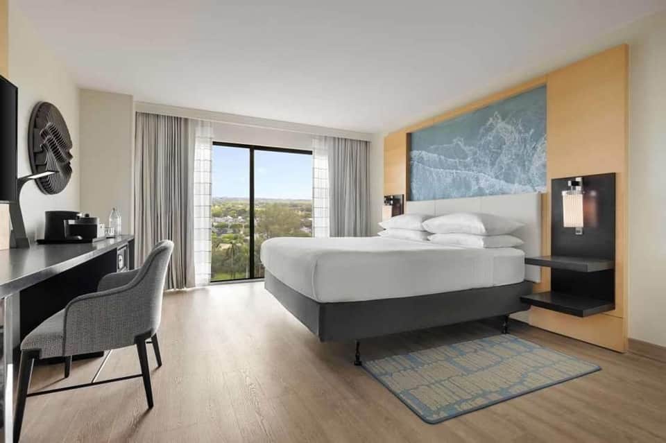Modern hotel bedroom with king bed, work desk, balcony with panoramic views, and contemporary decor