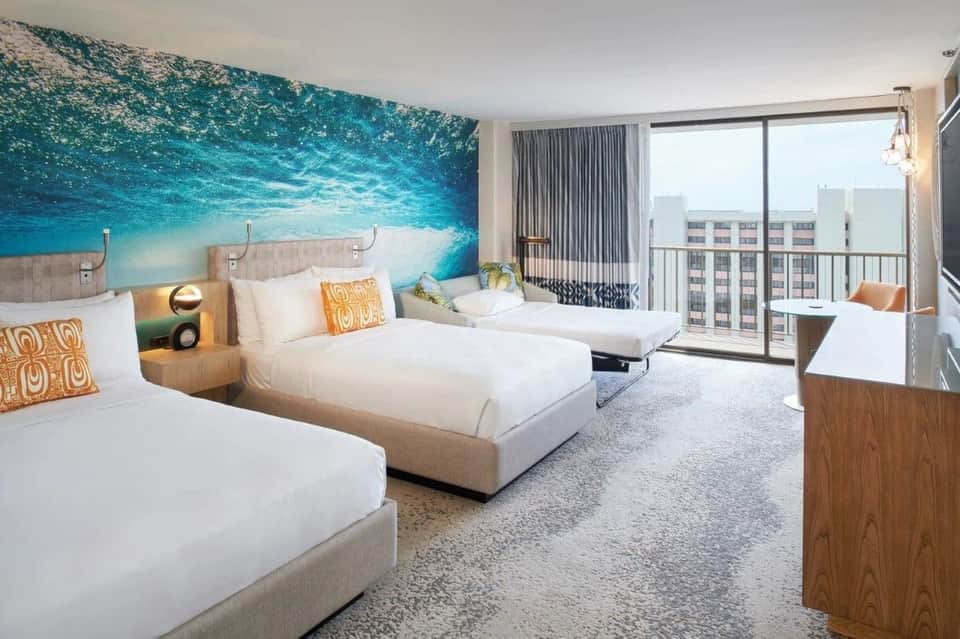 Beachfront hotel room with two beds, ocean mural headboard, and ocean view balcony