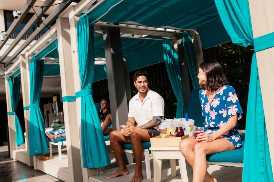 Guests enjoying drinks in turquoise cabanas with curtains and lounge seating