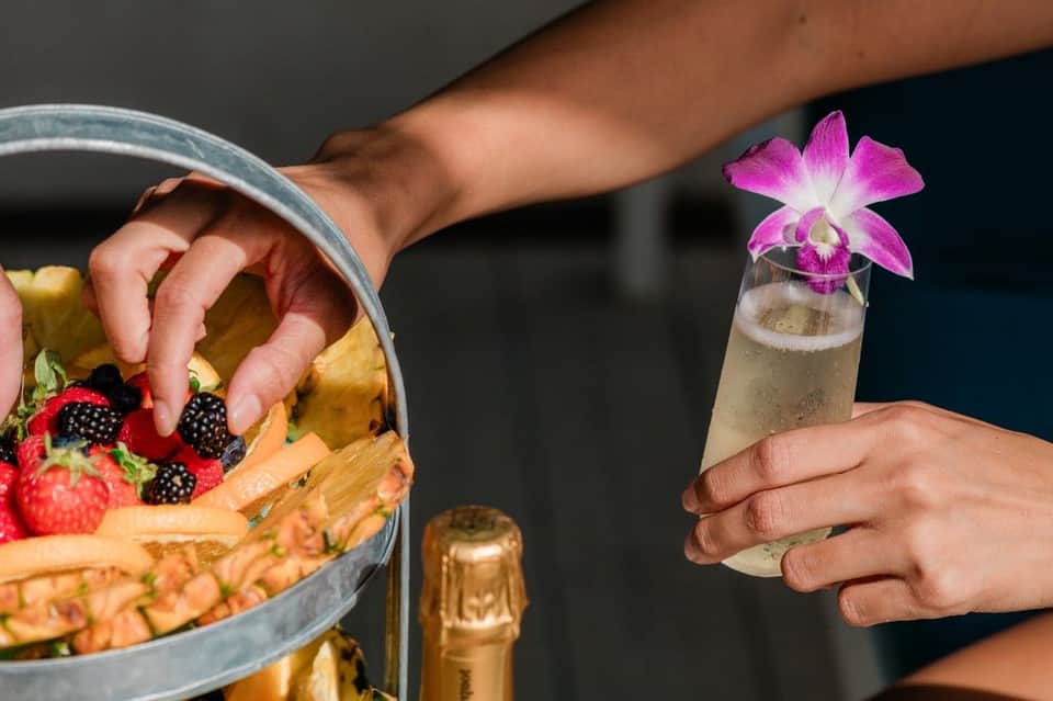Hand holding champagne flute with orchid flower next to golden basket of fresh berries