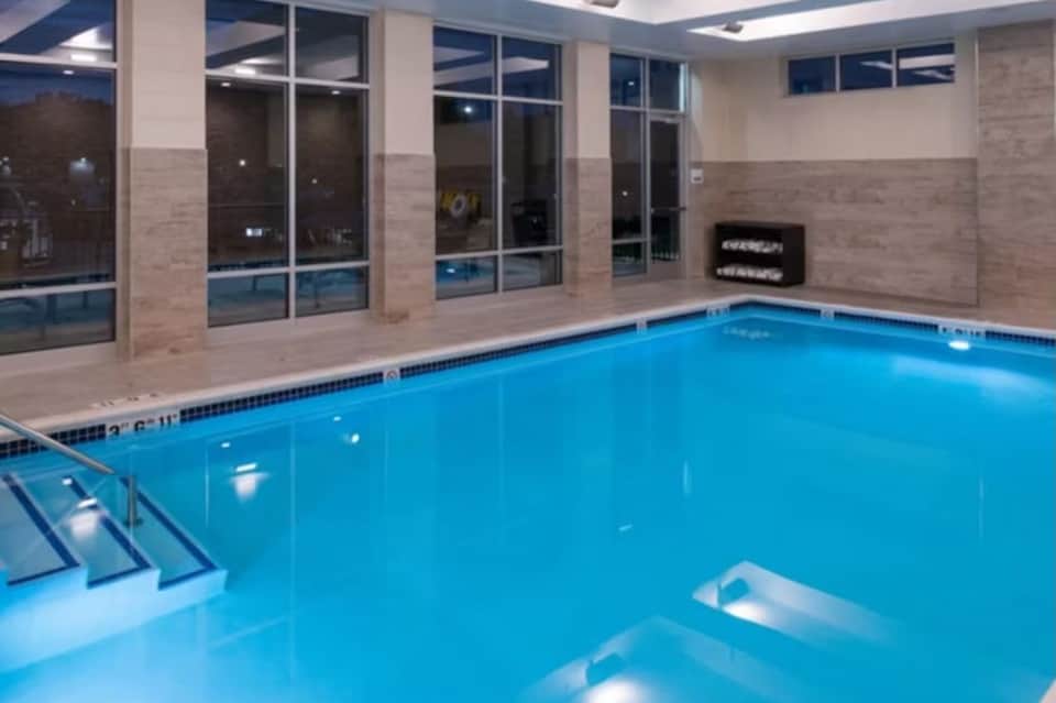 Indoor heated swimming pool with blue water, brick walls, large windows, and entry steps visible