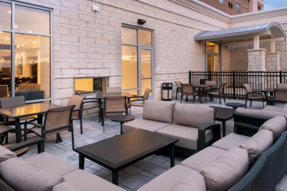 Outdoor patio with lounge seating, fire pit, dining tables, and modern building exterior at dusk