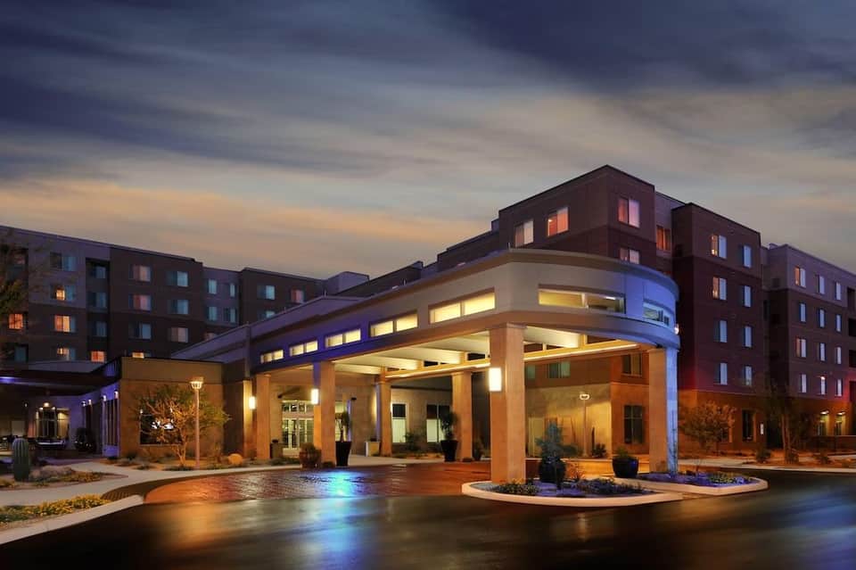 Modern hotel entrance with contemporary architecture, blue accent lighting, and residential towers at dusk