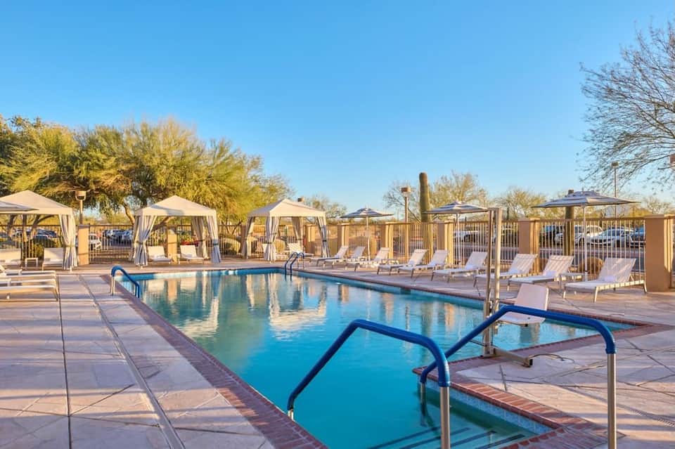 Resort pool with loungers and cabanas under clear blue sky surrounded by desert landscaping