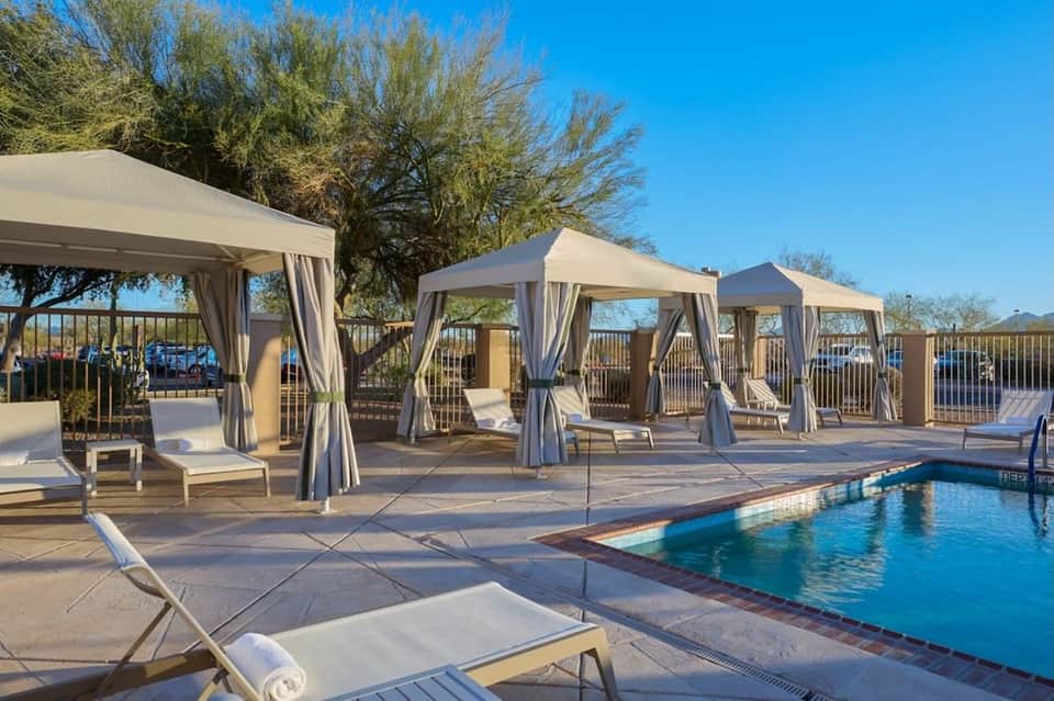 Pool area with multiple cabanas featuring white curtains and lounge chairs by the water