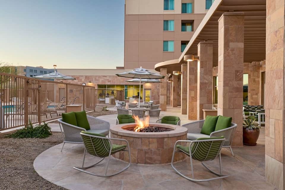 Outdoor firepit lounge area with green cushioned rocking chairs and stone architectural elements