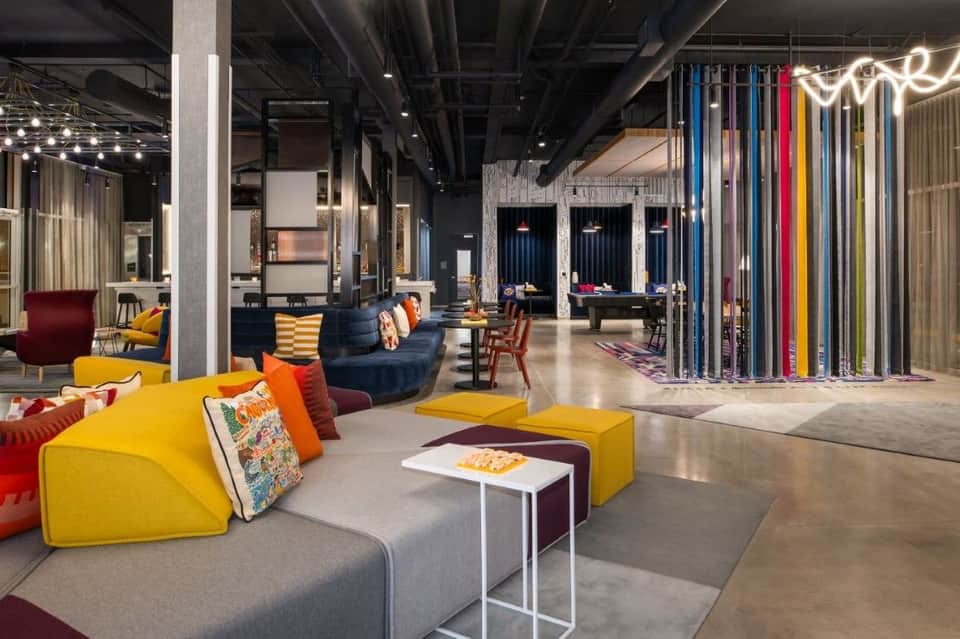 Modern hotel lounge with yellow modular seating, colorful accent pillows, dark blue furniture, and vibrant neon signage