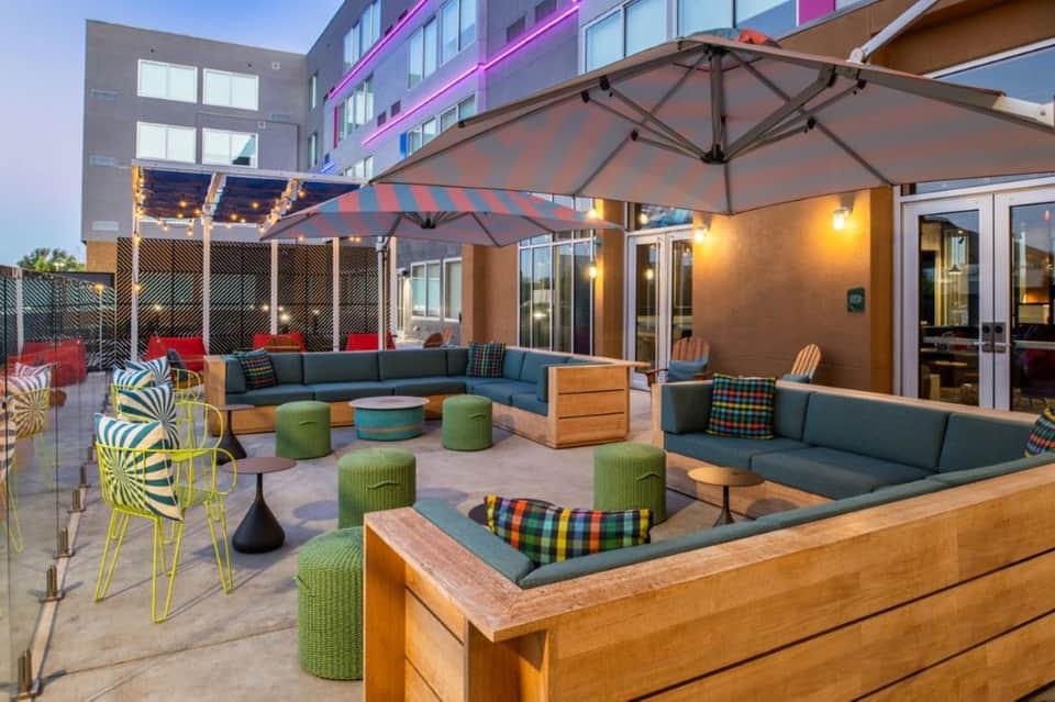 Rooftop terrace with turquoise pool, blue lounge seating, green poufs, striped umbrellas, and colorful patterned pillows