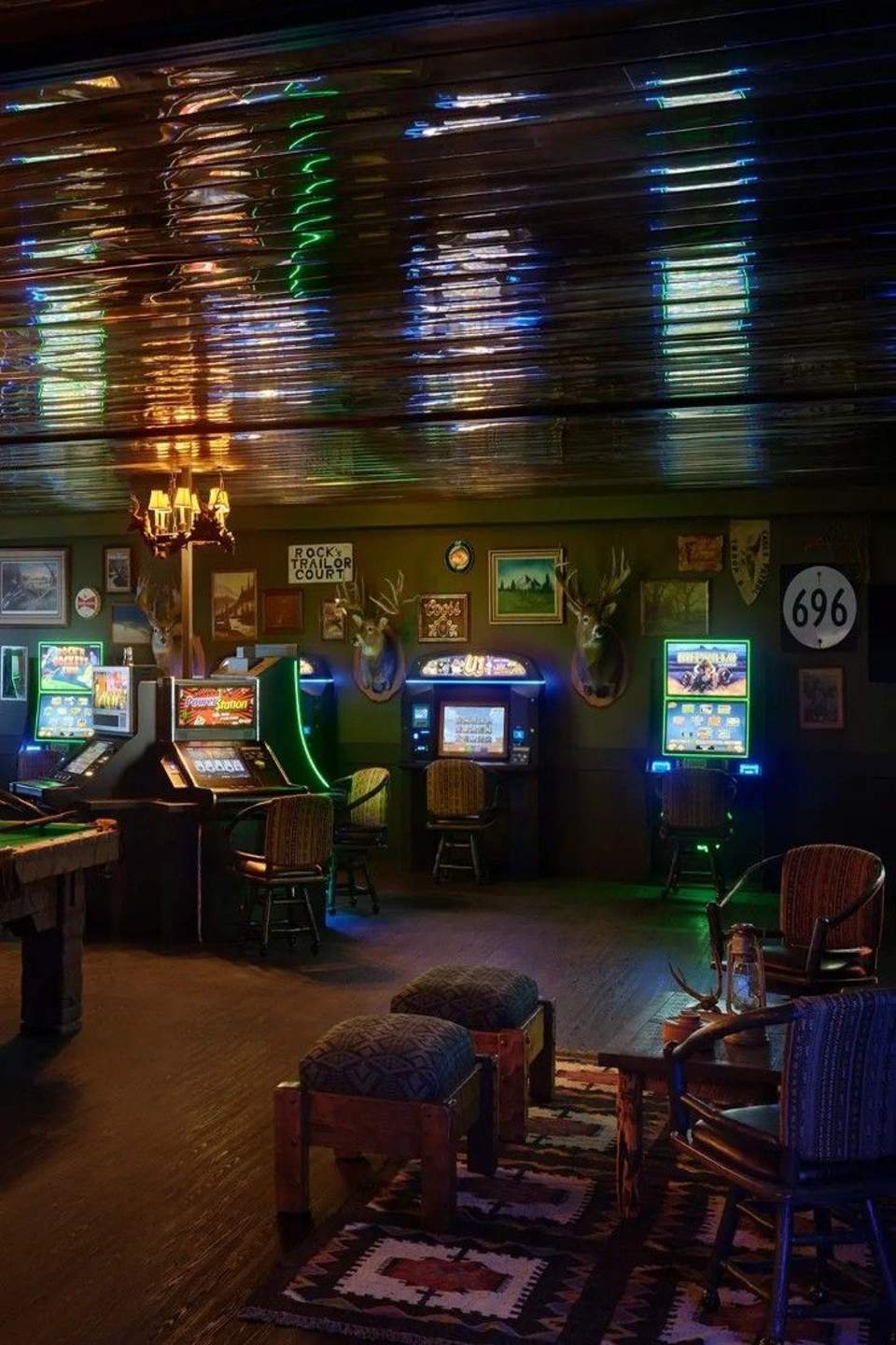Dimly lit game room with neon signs, slot machines, mounted antlers, and retro Americana decor