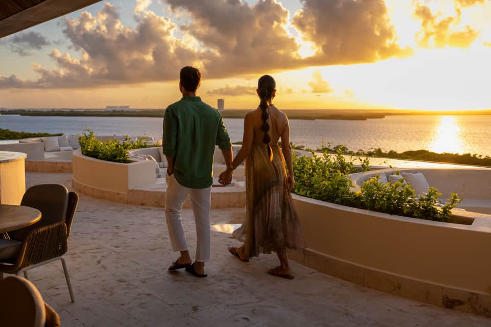 Couple holding hands on terrace overlooking bay at golden sunset with landscaping