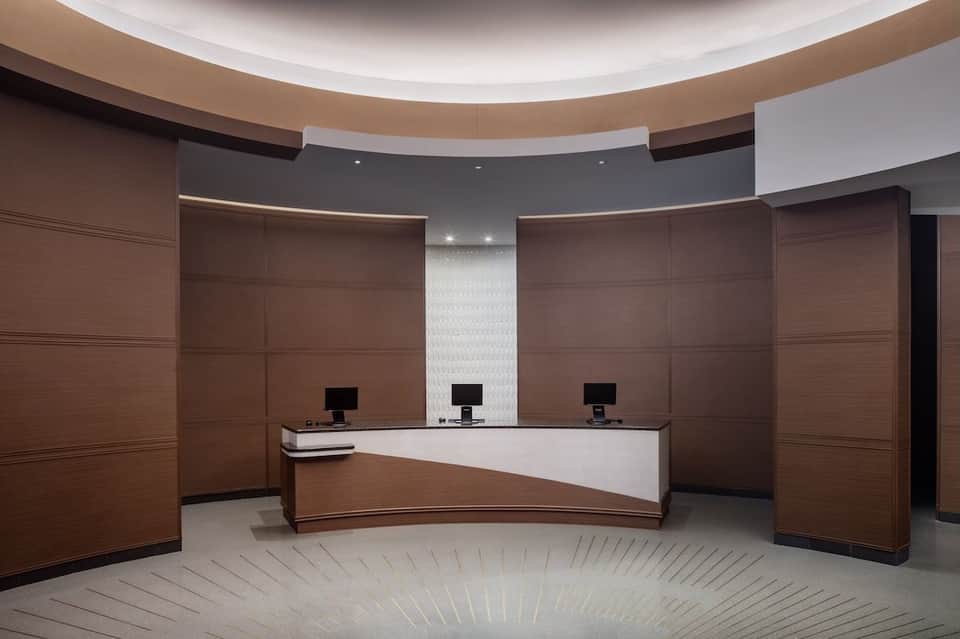Modern hotel reception desk with curved white counter, dark wood paneling, and three computer stations in circular room