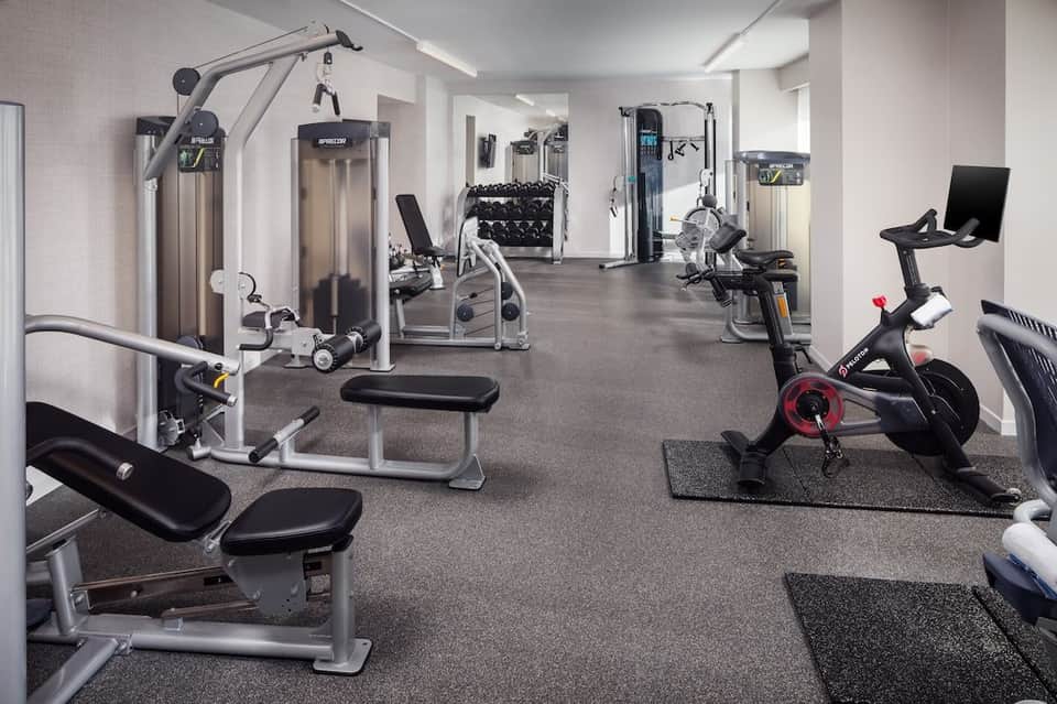 Spacious fitness center with cardio machines, weight equipment, exercise bikes, and dumbbells on gray flooring