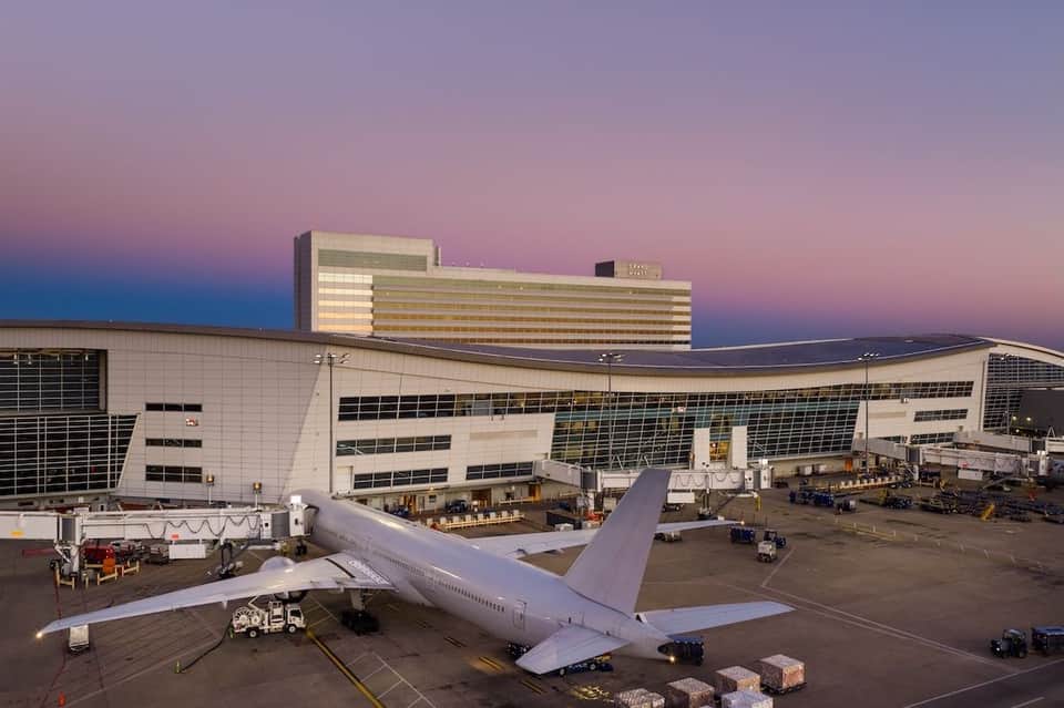 Commercial aircraft parked at airport terminal gate with modern hotel building illuminated at dusk