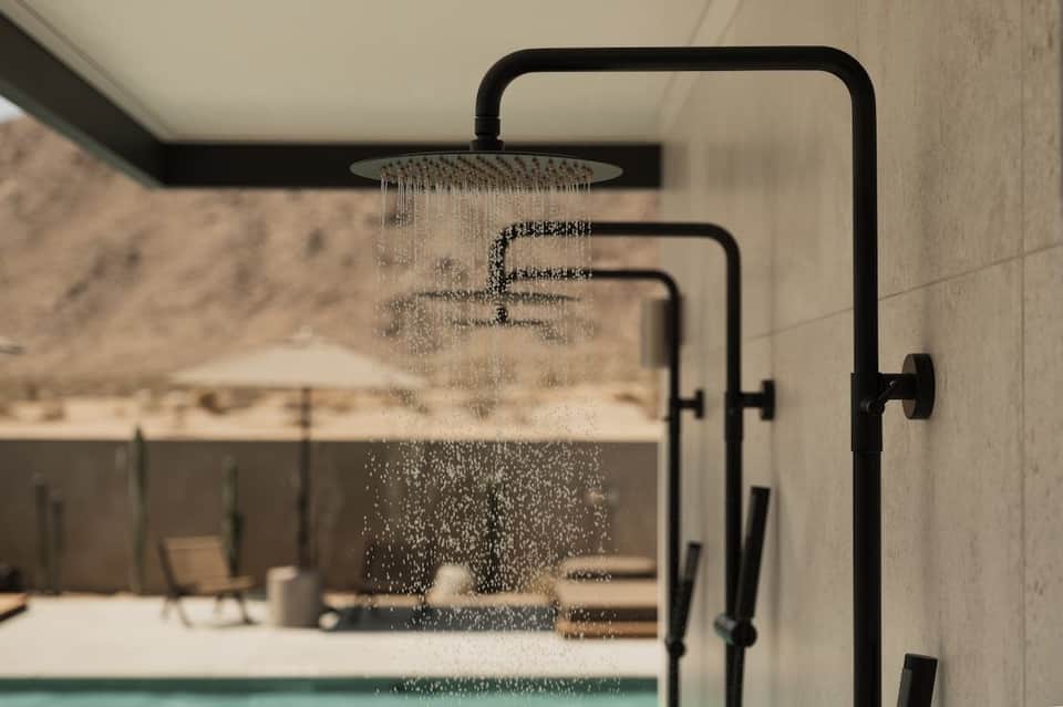 Black rainfall showerhead with cascading water in a modern bathroom overlooking a desert landscape