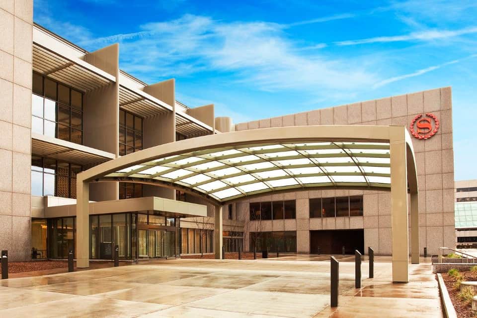 Modern hotel entrance with curved glass canopy and beige stone facade under blue sky