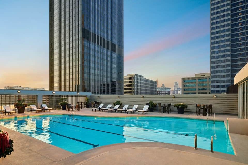 Rooftop swimming pool with city skyline views, lounge chairs, and tall buildings