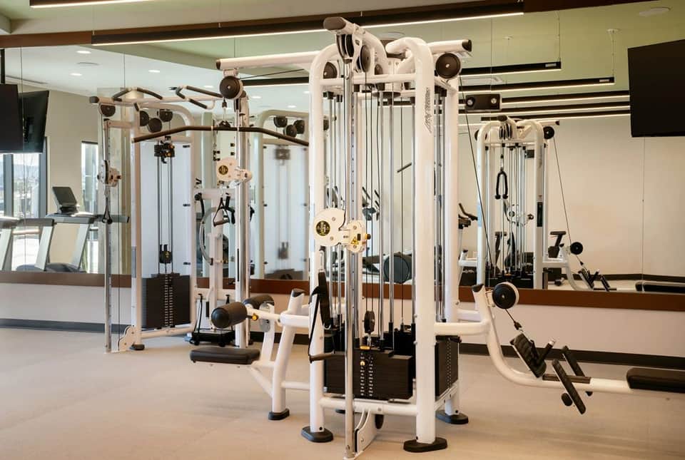 Multi-station strength training equipment with white frame and mirrors in a bright, contemporary gym facility