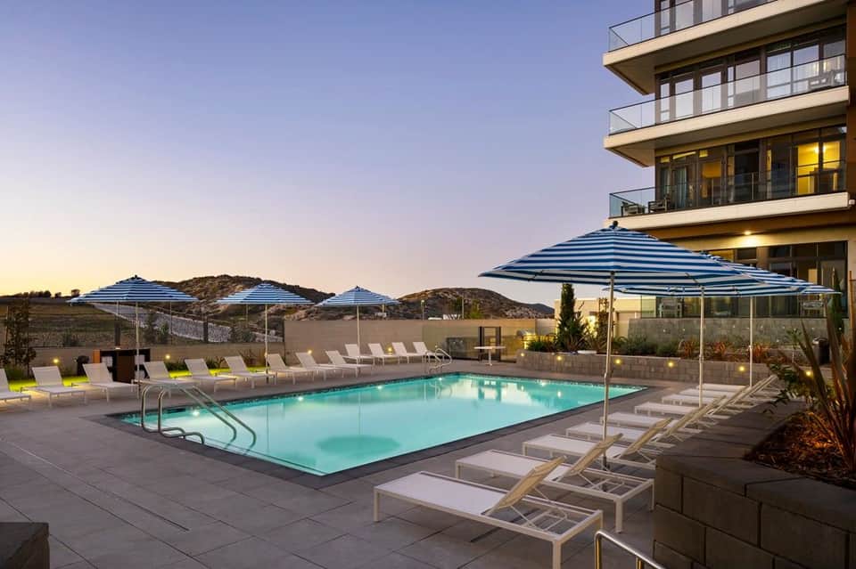 Resort pool with blue umbrellas and lounge chairs at dusk, modern building in background