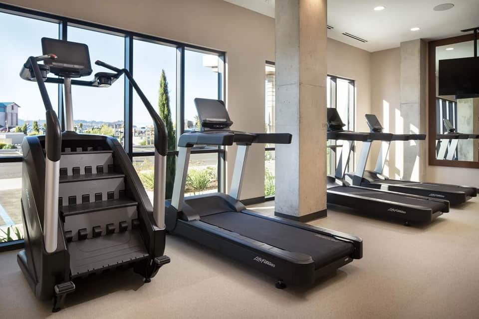 Modern fitness center with treadmills, stationary bikes, and large windows overlooking landscape