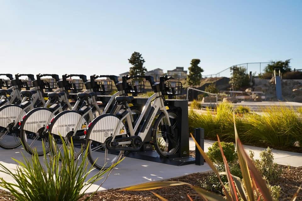 Row of black and white electric bikes parked in outdoor bike-sharing station with landscaping