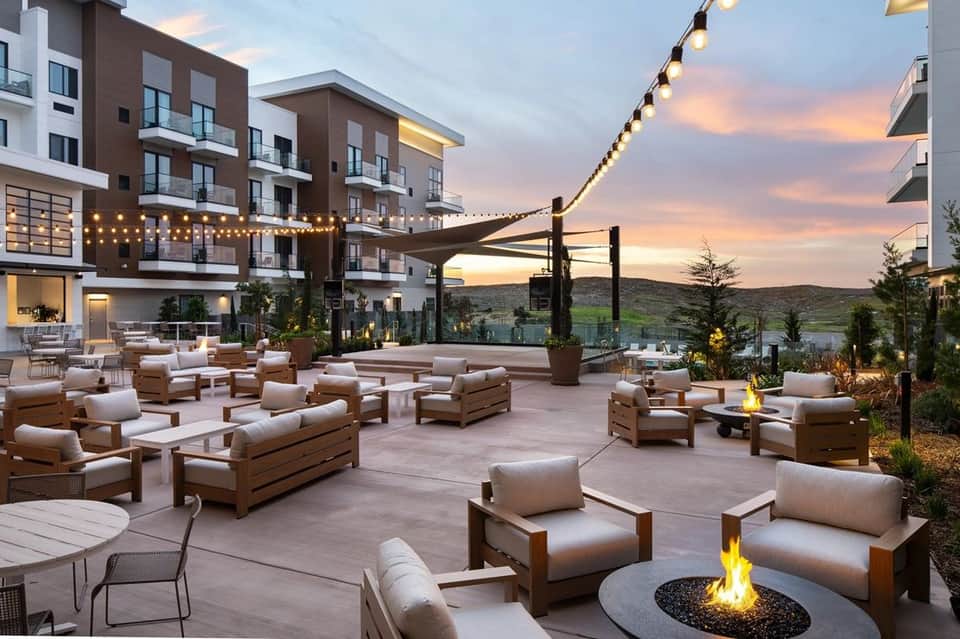 Outdoor lounge area with beige seating, fire pit, string lights, and sunset mountain views