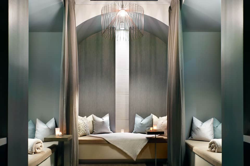 Luxurious bedroom alcove with grey upholstered walls, white pillows, and modern geometric ceiling fixture