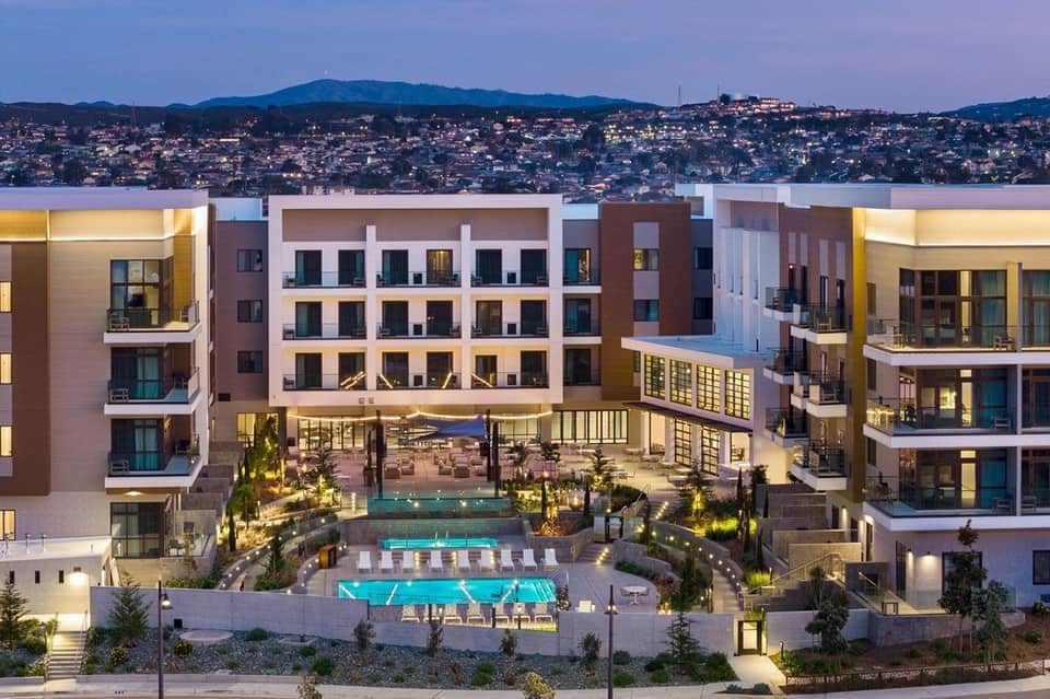 Aerial view of resort pools and courtyard lit at night with surrounding apartment towers