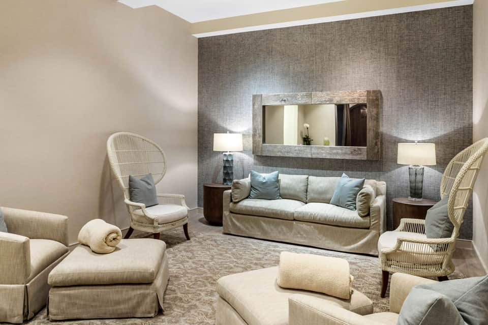 Elegant spa lounge with cream furnishings, woven chairs, and mirror accent wall