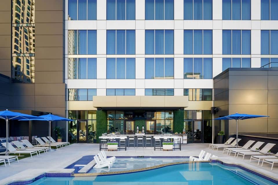Modern hotel courtyard with swimming pool, lounge chairs, blue umbrellas, and contemporary building facade