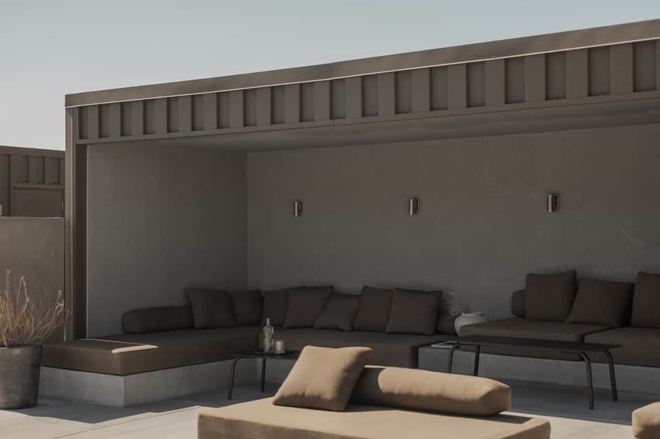 Modern outdoor seating area with dark sofas, beige pillows, and minimalist architectural design
