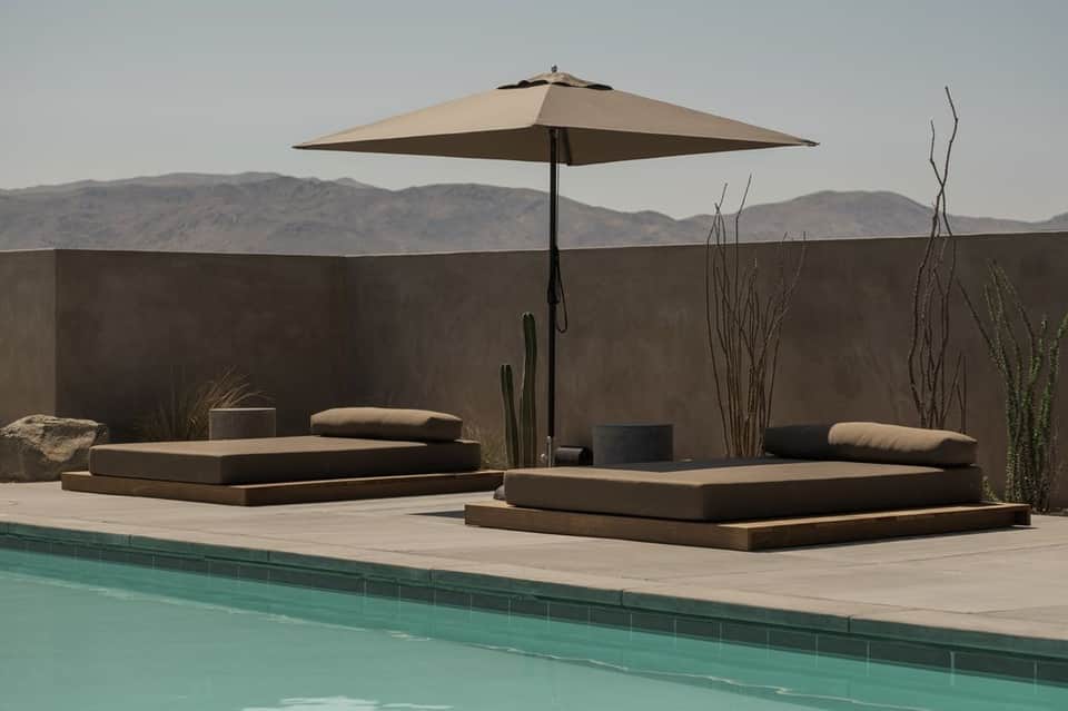 Poolside lounge with low platform seating, umbrella, desert landscape view, and architectural landscaping