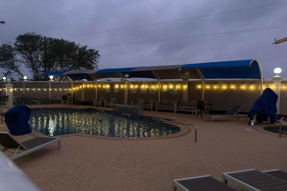 Outdoor pool with illuminated cabanas and lounge chairs at dusk