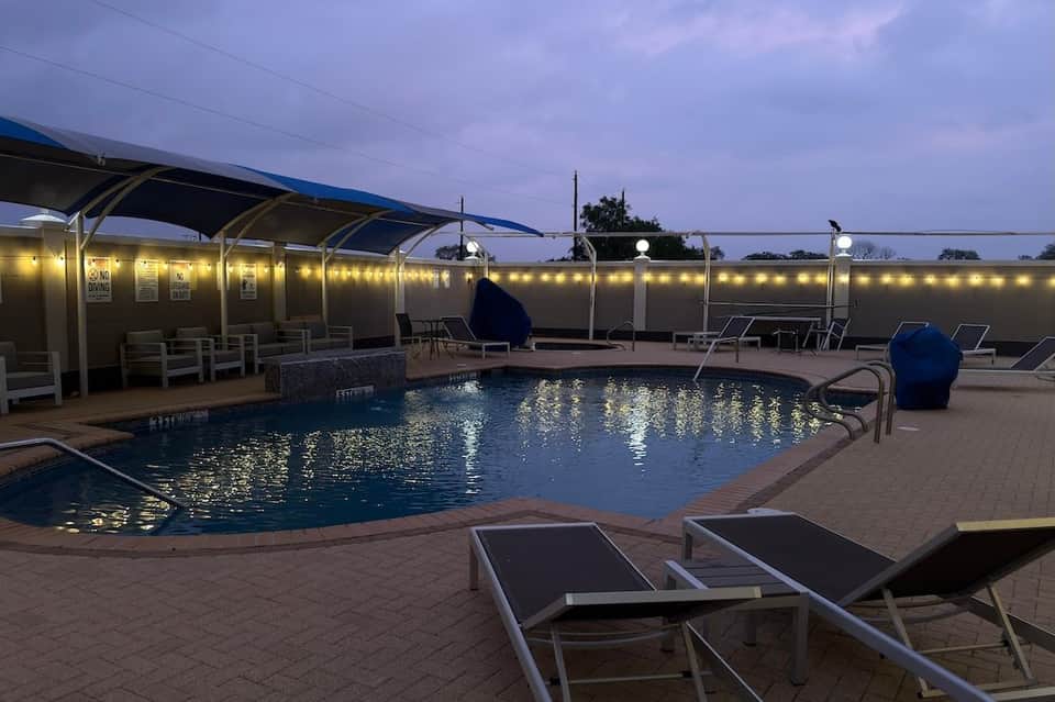 Curved pool with cabanas, lounge chairs, and evening lighting