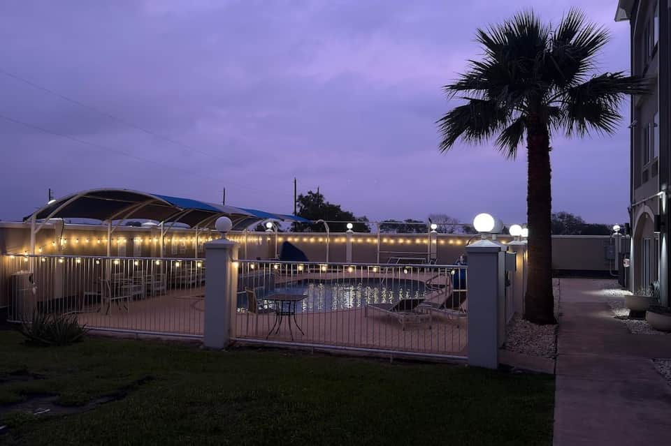 Gated pool area with palm tree, cabanas, and ambient lighting at twilight