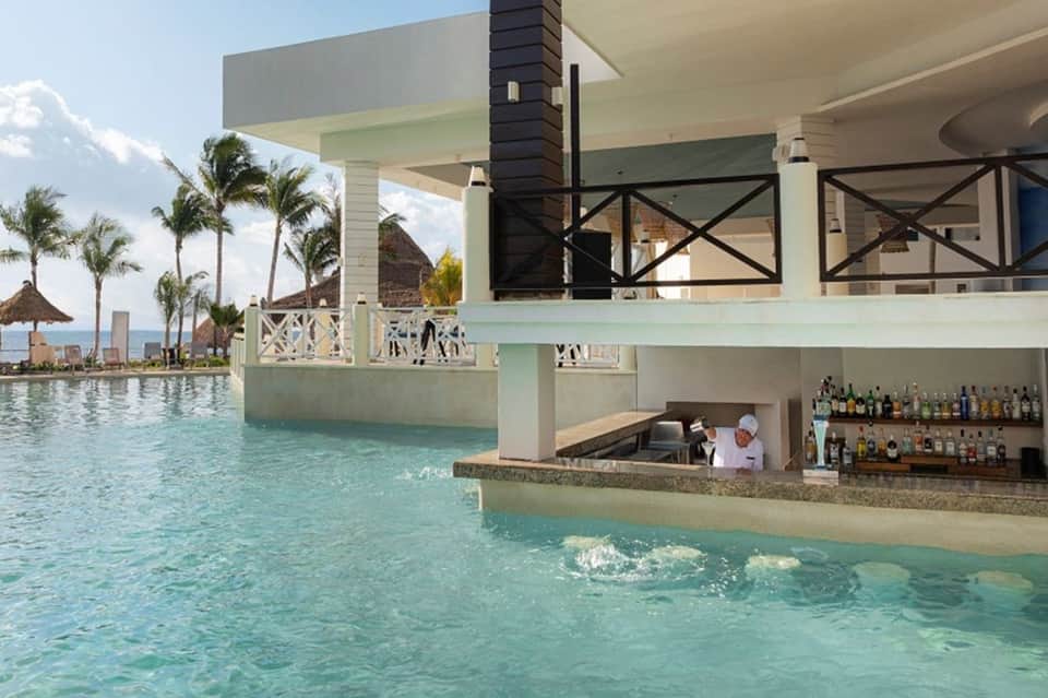 Modern pool bar with turquoise water, white architecture, palm trees, and ocean horizon view
