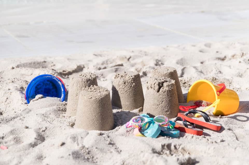 Beach sand with colorful children's toys including buckets, shovels, and sand molds scattered across the shore