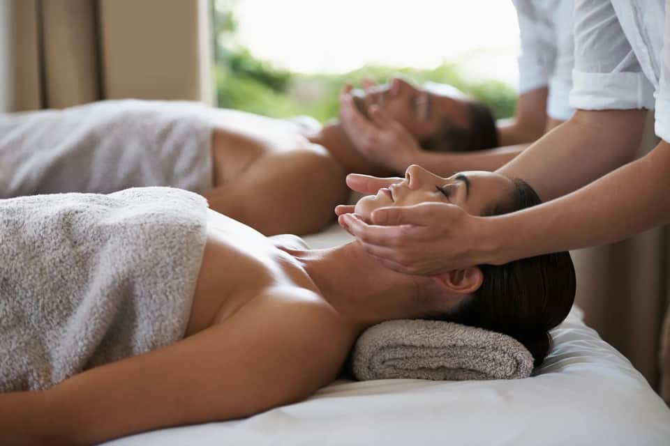 Spa therapist giving facial massage to relaxed client on massage bed with towel