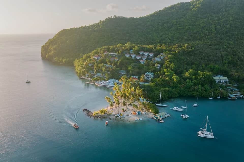 Aerial view of tropical beachfront resort nestled in lush jungle with sailboats anchored offshore
