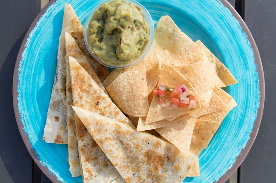 Crispy tortilla chips with guacamole dip and pico de gallo on turquoise plate