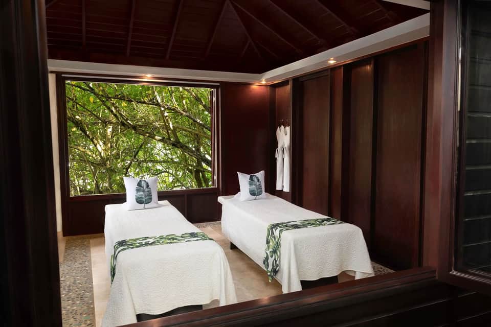 Twin beds in tropical wooden room with forest view, white linens, and botanical-inspired decor