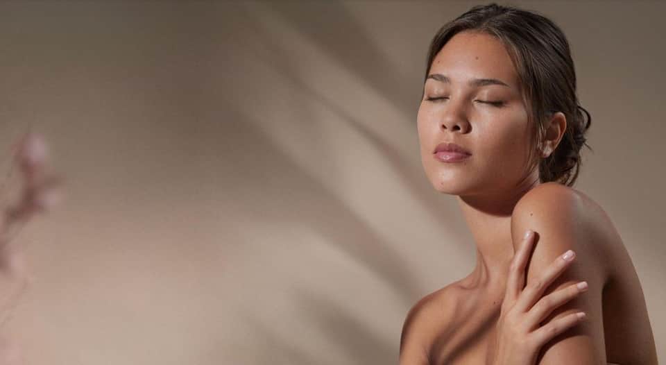 Woman in spa setting with natural lighting and neutral toned walls, peaceful atmosphere