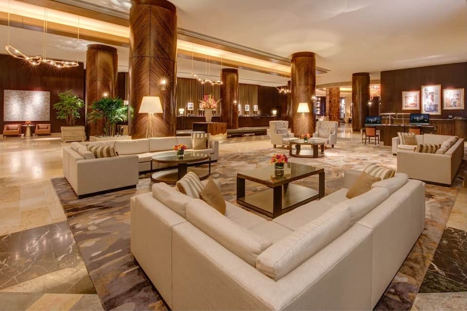 Luxury hotel lobby featuring marble floors, wooden columns, cream seating areas, and contemporary artwork
