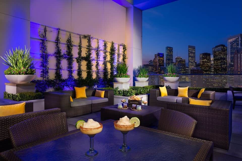 Modern rooftop lounge with purple lighting, living walls, and city skyline view at dusk