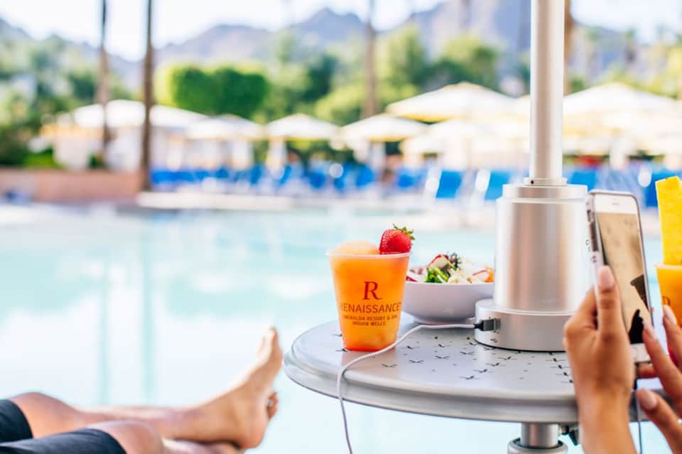 Orange cocktail with strawberry garnish on umbrella table overlooking resort pool