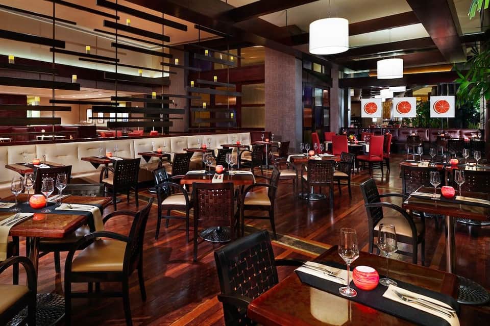 Contemporary restaurant with red and cream accents, geometric ceiling design, and dining tables