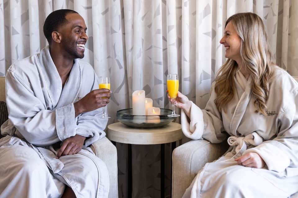 Couple in white robes toasting with champagne by candlelight in elegant room setting